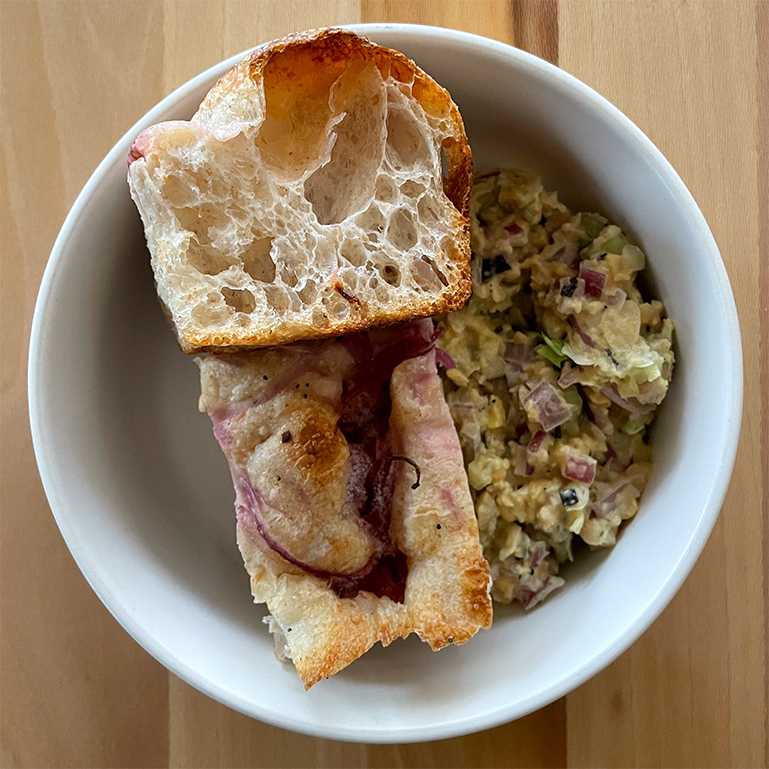 Slices of red onion and herb focaccia in a bowl with chickpea salad
